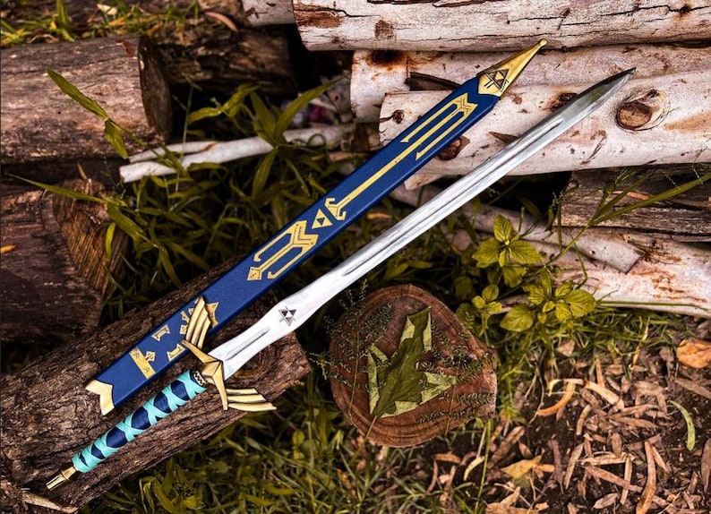 K&ouml;nnte beinhalten: Ein silbernfarbenes Schwert mit blau-goldfarbenem Griff und einer passenden blauen Scheide mit goldenen Akzenten. Das Schwert liegt auf einem Bett aus Holz und Gr&uuml;n, das eine Waffe im Fantasy-Stil zeigt.
