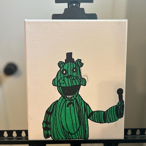 May include: A canvas painting featuring a green character with black stripes, a top hat, and a microphone. The character has a wide grin and is set against a white background. The artwork is displayed on a black easel.