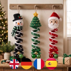 Op de afbeelding: Drie hangende gehaakte kerstversieringen met een sneeuwpop met een zwarte hoge hoed, een groene kerstboom met een gele ster en een kerstmanhoofd. Elk ornament heeft een spiraalvormig lichaam, een satijnen strik en twee hangende kerstballen.