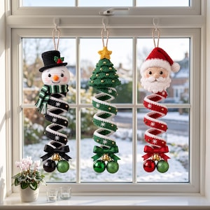 May include: Three hanging crochet Christmas decorations featuring a snowman in a black hat, a green Christmas tree with a yellow star, and a Santa Claus figure. Each ornament has a spiral body with snowflake patterns, a bow, and two baubles.