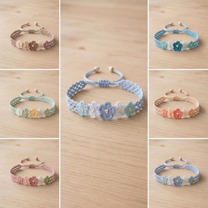 Peut inclure: Une collection de sept bracelets réglables ornés de motifs de fleurs au crochet. Chaque bracelet est composé d'une bande tissée et d'une série de petites formes florales délicates dans diverses palettes de couleurs, incluant des tons bleus, roses, beiges et verts.