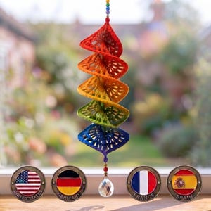 Op de afbeelding: Een hangende spiraaldecoratie gemaakt van gehaakte driehoekige segmenten in een regenboogverloop van rood, oranje, geel, groen en blauw. Een heldere gefacetteerde kristallen kraal hangt onderaan en kleine gekleurde kralen sieren de bovenkant.