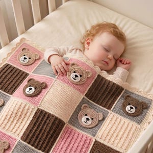 Op de afbeelding: Een gehaakte babydeken met een raster van vierkante vlakken in de kleuren roze, grijs, crème en donkerbruin. Verschillende vlakken zijn versierd met ronde, driedimensionale gehaakte berengezichtjes met geborduurde ogen en neuzen.