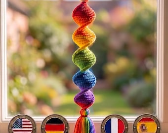 May include: A hanging crochet ornament featuring a vertical spiral of five spheres in red, orange, yellow, green, blue, and purple, topped with a wooden bead and finished with a multi-colored tassel, positioned above four circular metal flag tokens.
