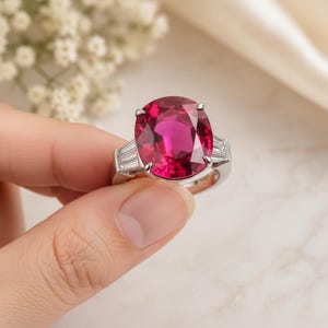 Puede incluir: Un anillo de plata con una gran gema roja vibrante de talla ovalada. El anillo est&aacute; flanqueado por dos gemas m&aacute;s peque&ntilde;as, rectangulares y transparentes a cada lado. El engaste es de dise&ntilde;o cl&aacute;sico, destacando la piedra central.