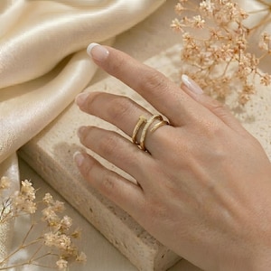 Puede incluir: Un anillo dorado con un diseño único, con una forma curva y pequeños adornos brillantes. El anillo se lleva en un dedo, mostrando sus intrincados detalles y su estilo elegante. El anillo parece estar hecho de metal y es una joya.