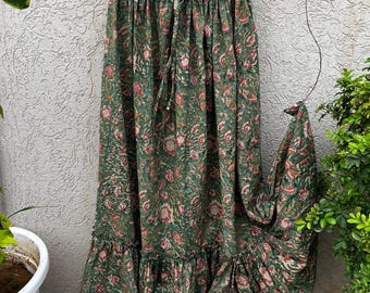 May include: A floor-length green skirt featuring a repeating floral pattern in shades of pink and white. The skirt has an elasticated waistband with a drawstring tie and a gathered tiered hemline that creates a full, flowing silhouette.