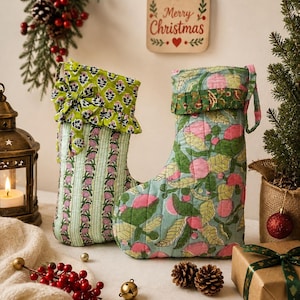 May include: Two quilted fabric Christmas stockings. The left stocking features a green and white vertical striped pattern with a floral cuff and bow. The right stocking displays a light blue background with a pink and green botanical fruit print.