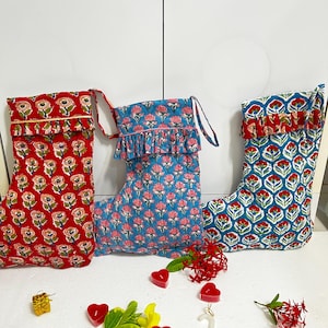 Puede incluir: Tres calcetines de tela acolchada con estampados florales. El calcetín de la izquierda es rojo con flores rosas y verdes, el central es azul con flores rosas y el de la derecha es azul con un motivo floral repetitivo en rojo y verde.