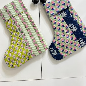 Op de afbeelding: Twee gewatteerde kerstsokken met geblokte bloemenprints. De linker kerstsok heeft groen-witte strepen met roze bloemen, terwijl de rechter kerstsok lichtgroene bloemenstof combineert met donkerblauwe panelen en witte motieven.
