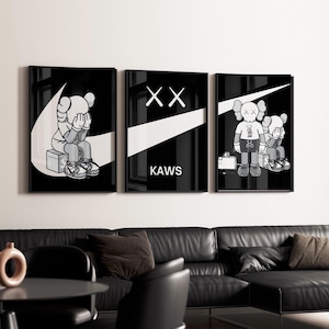 Peut inclure: Ensemble de trois impressions d'art KAWS en noir et blanc encadrées. Chaque impression présente un personnage KAWS avec les yeux XX emblématiques, sur fond noir avec des accents blancs. Le mot "KAWS" est en blanc sur l'impression du milieu.