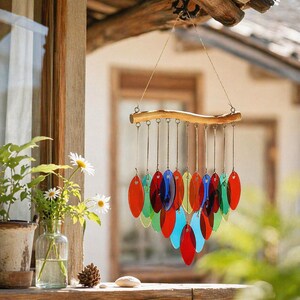 May include: A colorful wind chime with a wooden bar and hanging, oval-shaped glass pieces in shades of red, blue, green, and yellow. The chime is suspended from a natural wood beam, creating a decorative outdoor accent.