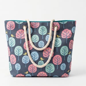 May include: A tote bag with a navy blue background featuring a repeating pattern of colorful trees and small yellow birds. The bag has a teal interior and rope handles. The bag is approximately 15 inches wide and 12 inches tall.