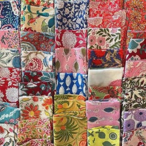 Puede incluir: Una colección de cuadrados de tela doblados en varios colores y patrones. Las telas presentan diseños florales, de hojas y geométricos en tonos de rojo, azul, rosa, amarillo y verde. Los textiles están cuidadosamente apilados, mostrando una variedad de estampados.