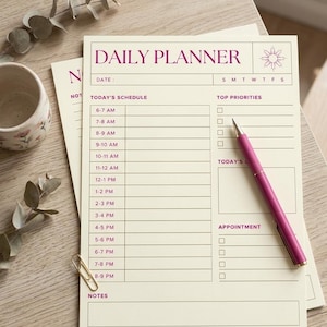 May include: A daily planner with the words "DAILY PLANNER" in purple. The planner has sections for scheduling, top priorities, and appointments. A purple pen rests on the planner, and a gold paperclip is visible.