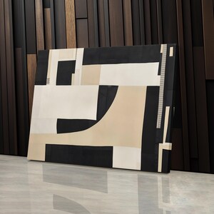 May include: A rectangular canvas wall art piece featuring a geometric composition of black, white, and beige shapes. The design consists of solid blocks and intersecting lines, creating a structured arrangement of contrasting colors and sharp angles.