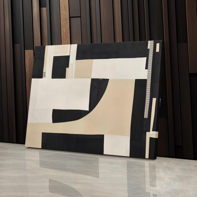 May include: A rectangular canvas wall art piece featuring a geometric composition of black, white, and beige shapes. The design consists of solid blocks and intersecting lines, creating a structured arrangement of contrasting colors and sharp angles.