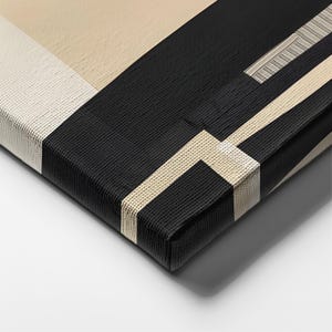 May include: A canvas print featuring a geometric composition of black, beige, and off-white blocks. The design includes sharp, intersecting lines and a textured surface that wraps around the edges of the rectangular frame, creating a clean visual.