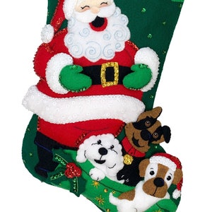 May include: Handmade Christmas stocking featuring Santa Claus and three dogs. The stocking is green with red and white accents, and the name "QUINN" is embroidered in red. The Santa Claus figure is wearing a red suit and hat, and the dogs are various breeds.