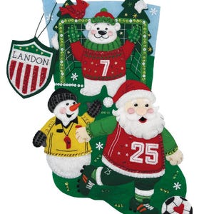 Op de afbeelding: Een kerstsok met een voetbalthema. De sok toont een ijsbeer, een sneeuwpop en de kerstman die voetbal spelen. De sok is groen met een blauwe bovenkant en een schild met de tekst "LANDON".