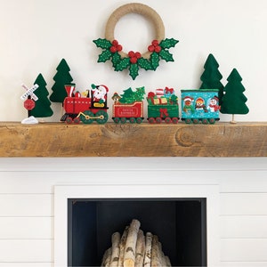 May include: A Christmas-themed display featuring a felt train set with Santa Claus, a Christmas tree, and gifts. The train cars are red, green, and blue, with the words "Santa Express" on one car. A holly wreath and felt Christmas trees complete the festive scene.