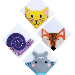 Op de afbeelding: Vier vilten dierenpatches: een gele kat, een bruine en oranje vos, een paarse slak en een grijze nijlpaard. Elk dier staat op een witte vierkant met decoratieve pailletten. De kat heeft zwarte snorharen en een lachend gezicht.