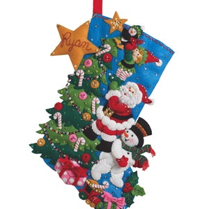 Könnte beinhalten: Ein handgefertigter Weihnachtsstrumpf mit blauem Hintergrund und festlichen Dekorationen. Er zeigt einen Weihnachtsbaum aus Filz, den Weihnachtsmann, einen Schneemann und einen Stern mit dem Namen "Ryan". Der Strumpf ist mit Pailletten und Zuckerstangen verziert.