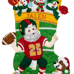 Peut inclure: Une chaussette de Noël sur le thème du football, avec le Père Noël, des bonhommes de neige et un chien. La chaussette est verte et jaune, avec le nom "JALEN". Le Père Noël porte un maillot rouge avec le numéro 25.