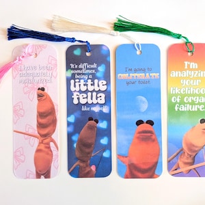 May include: Four colorful bookmarks with tassel accents. Each bookmark features a cartoon character and humorous text. The bookmarks have pink, blue, white, and green tassels. The text includes phrases like "I'm analyzing your likelihood of organ failure."