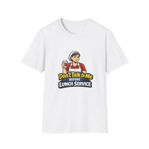 Puede incluir: Camiseta blanca con un gráfico de una mujer con una parte superior roja y un delantal blanco sosteniendo una taza de café. El texto "Don't Talk to Me Before Lunch Service" se muestra en amarillo y negro.