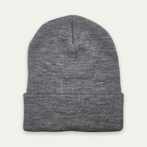 May include: A charcoal gray knit beanie cap featuring a classic cuffed design. The hat is constructed from a soft, textured yarn with a visible ribbed knit pattern throughout, providing a simple and functional head covering for cold weather.