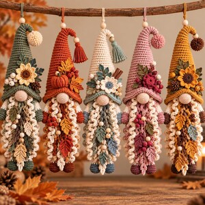 Peut inclure: Cinq décorations suspendues en forme de gnomes au crochet aux couleurs automnales. Chaque gnome possède un chapeau pointu orné de fleurs, feuilles, baies ou citrouilles en crochet, un nez rond et une longue barbe texturée avec des perles.
