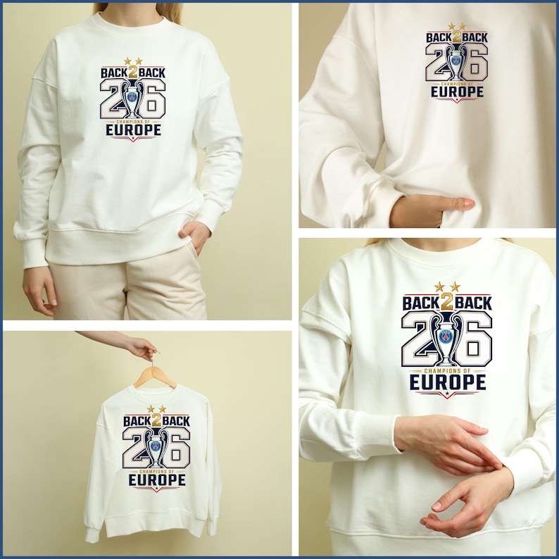 Pode incluir: Uma camisola branca de manga comprida com uma impress&atilde;o gr&aacute;fica que diz BACK 2 BACK 26 CHAMPIONS OF EUROPE, com um &iacute;cone de trof&eacute;u central, duas estrelas douradas por cima e detalhes em vermelho e azul no peito da pe&ccedil;a.