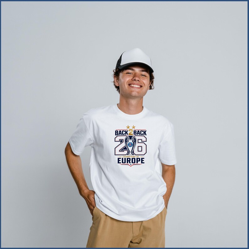 Pode incluir: Uma t-shirt branca com um gr&aacute;fico contendo o texto BACK 2 BACK, o n&uacute;mero 26 e CHAMPIONS OF EUROPE, juntamente com uma ilustra&ccedil;&atilde;o de um trof&eacute;u e duas estrelas douradas. A t-shirt &eacute; combinada com um bon&eacute; branco e preto e cal&ccedil;as bege.