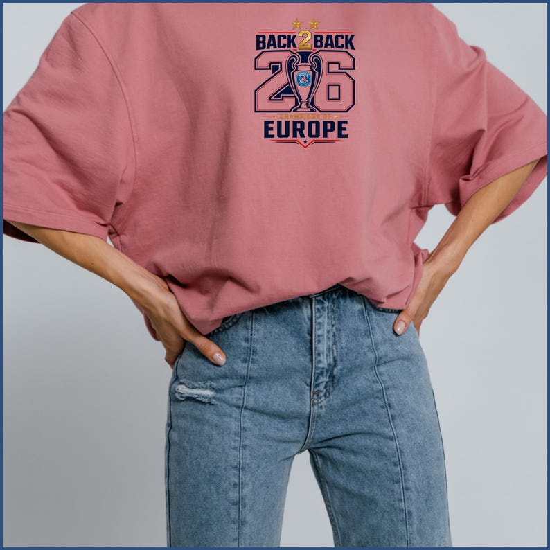 Pode incluir: Uma t-shirt de manga curta em rosa seco com uma impress&atilde;o gr&aacute;fica que diz BACK 2 BACK 26 EUROPE, um &iacute;cone de trof&eacute;u central e duas estrelas douradas. O design &eacute; impresso em azul-marinho, dourado e vermelho no peito da pe&ccedil;a.