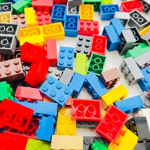 May include: A vibrant assortment of colorful plastic building blocks in various shapes and sizes. The blocks are primarily red, yellow, blue, green, and gray, with some brown and white pieces. The image shows a variety of blocks, including 2x2, 2x4, and other configurations.