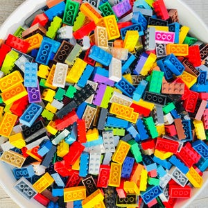May include: A bowl filled with a colorful assortment of plastic building blocks. The blocks are in various colors, including red, yellow, blue, green, and purple. The blocks are of different sizes and shapes, suitable for creative construction projects.