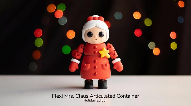 May include: An articulated figure of Mrs. Claus with white hair, a red coat, and a yellow star pin. The figure has black eyes, white cuffs, and black boots. Text at the bottom reads: Flexi Mrs. Claus Articulated Container Holiday Edition.