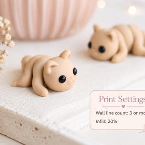 May include: Two small, tan-colored, handmade cat figurines with black eyes are lying on a white surface. The figurines are in a relaxed pose. The image also includes a blurred pink bowl and text that reads "Print Settings: Wall line count: 3 or more, Infill: 20%."