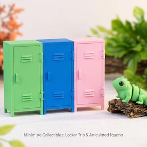 May include: A set of three miniature lockers in green, blue, and pink, each featuring vertical vents and a handle. Beside the lockers sits a small, light green articulated iguana figurine resting on a textured brown piece of wood.