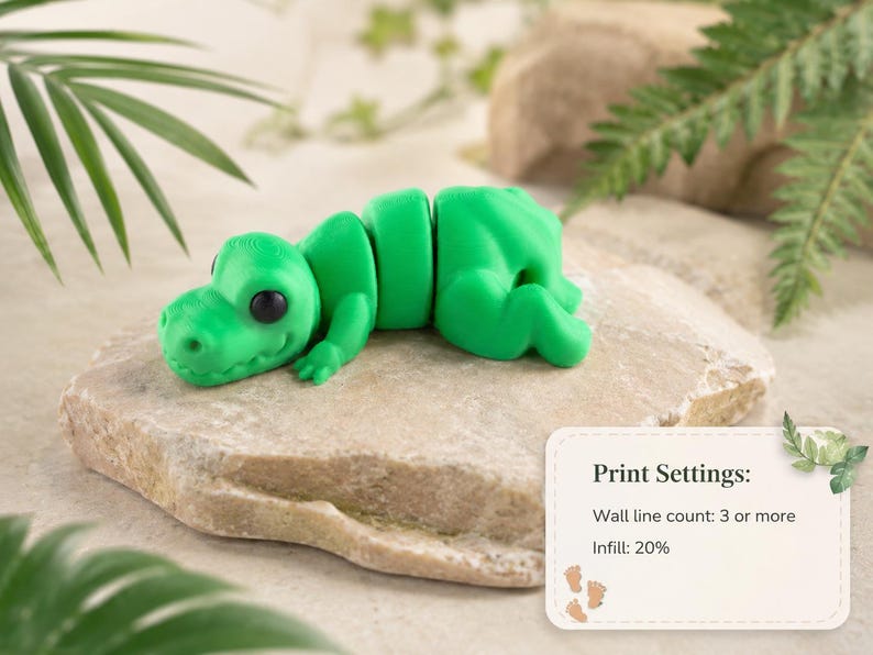 May include: A bright green articulated dinosaur toy with black eyes, resting on a light-colored stone. The toy is segmented, allowing for movement. The image includes a small card with print settings.