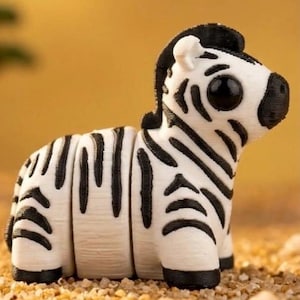 May include: A white and black zebra figurine with large black eyes. The zebra has black stripes and a black mane. The figurine is sitting on a bed of small, tan pebbles. The background is a solid, warm yellow.