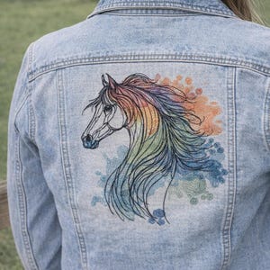 May include: Light blue denim jacket featuring an embroidered horse head design on the back. The horse's mane and surrounding details are in a rainbow of colors, including blue, orange, and green. The jacket has a classic denim style.
