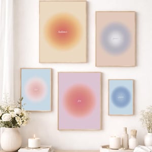 Op de afbeelding: Een verzameling ingelijste wandkunst met zachte, vage gradiëntontwerpen. Elk stuk heeft een centrale, cirkelvormige kleurengradiënt met woorden als "balans" en "vreugde" in het midden. De kleurenpaletten omvatten perzik, roze, blauw en lavendel.