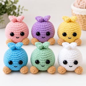 Può includere: Sei peluche rotondi all'uncinetto disposti su due file. Ogni giocattolo presenta un corpo sferico di colore rosa, viola, giallo, blu, verde o bianco, con due piccoli piedi color marrone chiaro, un nodo superiore e due occhi in plastica nera.
