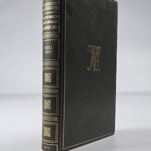 Puede incluir: Un libro de tapa dura negro con letras doradas y filigranas decorativas en el lomo y la portada. El texto del lomo dice Economisch Historisch Jaarboek, Deel XVII y 1931. Un monograma dorado está centrado en la portada del libro.