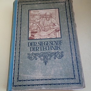 Puede incluir: Libro antiguo titulado "Der Siegeslauf Der Technik" con una cubierta azul y gris. La portada presenta una ilustración de un hombre y maquinaria, con detalles de borde ornamentados. El lomo del libro es azul.