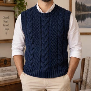 Op de afbeelding: Een marineblauw mouwloos vest met een opvallend verticaal kabelbreipatroon, een geribbelde ronde hals en geribbelde armsgaten en zoom. Het kledingstuk wordt gedragen over een wit overhemd met lange mouwen en een lichtbeige broek.