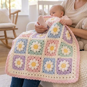 May include: A square crochet baby blanket featuring a repeating pattern of daisy motifs with yellow centers and white petals. The squares are bordered in pastel shades of pink, blue, green, and lavender, finished with a cream-colored crochet edge.