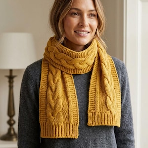 May include: A mustard yellow knit scarf featuring a prominent central cable knit pattern flanked by vertical ribbed sections. The scarf has a thick, textured construction with a ribbed hem at the ends, worn over a dark gray long-sleeve sweater.